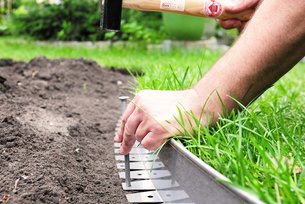 Galabauer fixiert die Beeteinfassung mit Erdankern damit die Rasenkante nicht absackt